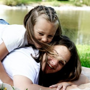 Petite fille riant sur le dos de sa maman, shooting famille à Saint-Hilaire-du-Harcouët en Normandie.